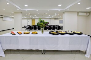 A conference room with a long table set for a buffet, surrounded by chairs, and a white ceiling with recessed lighting. - Hotel Domani (Guarulhos)