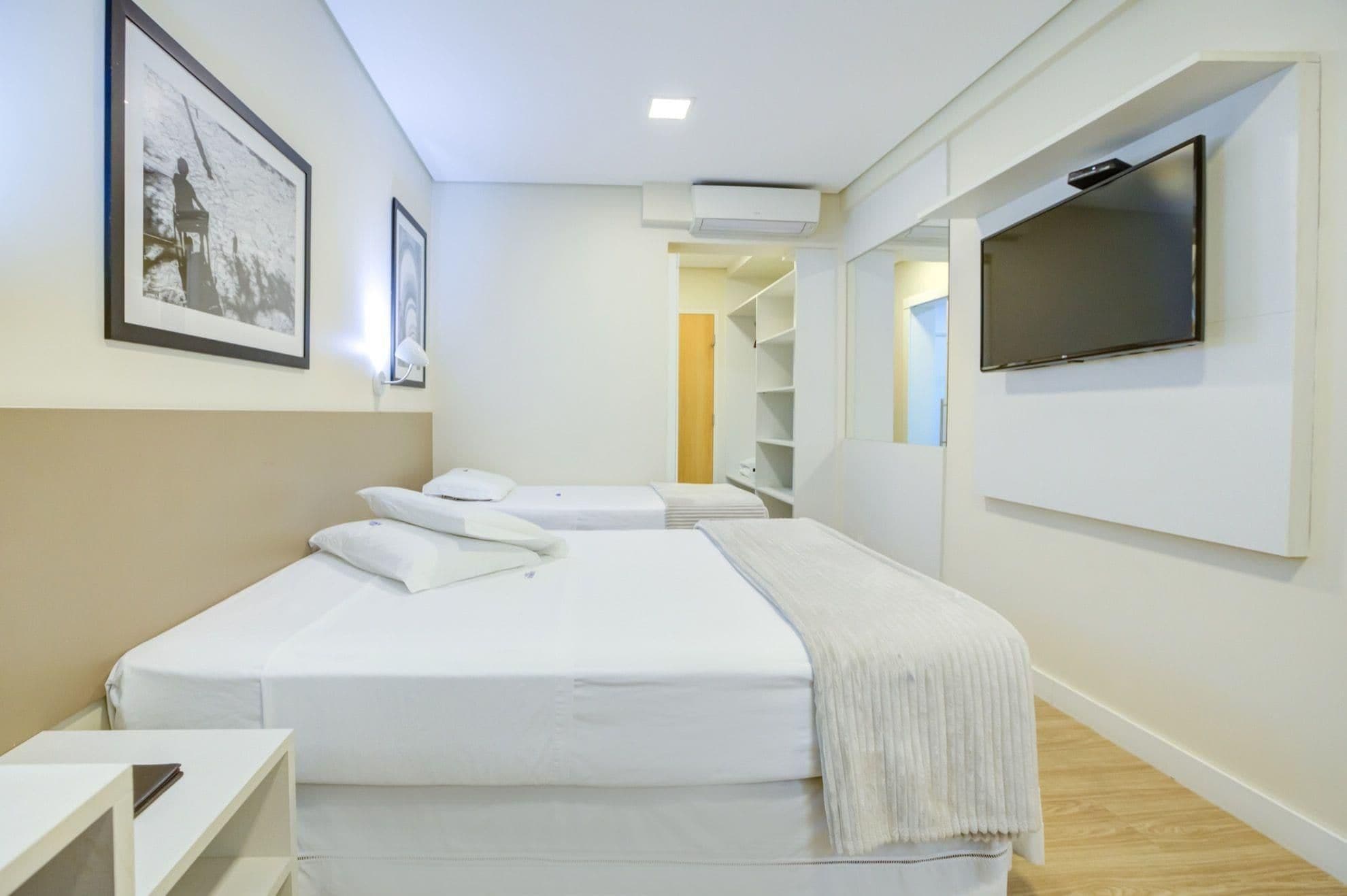 Una habitación de hotel con una cama, un televisor montado en la pared y un cuadro enmarcado.