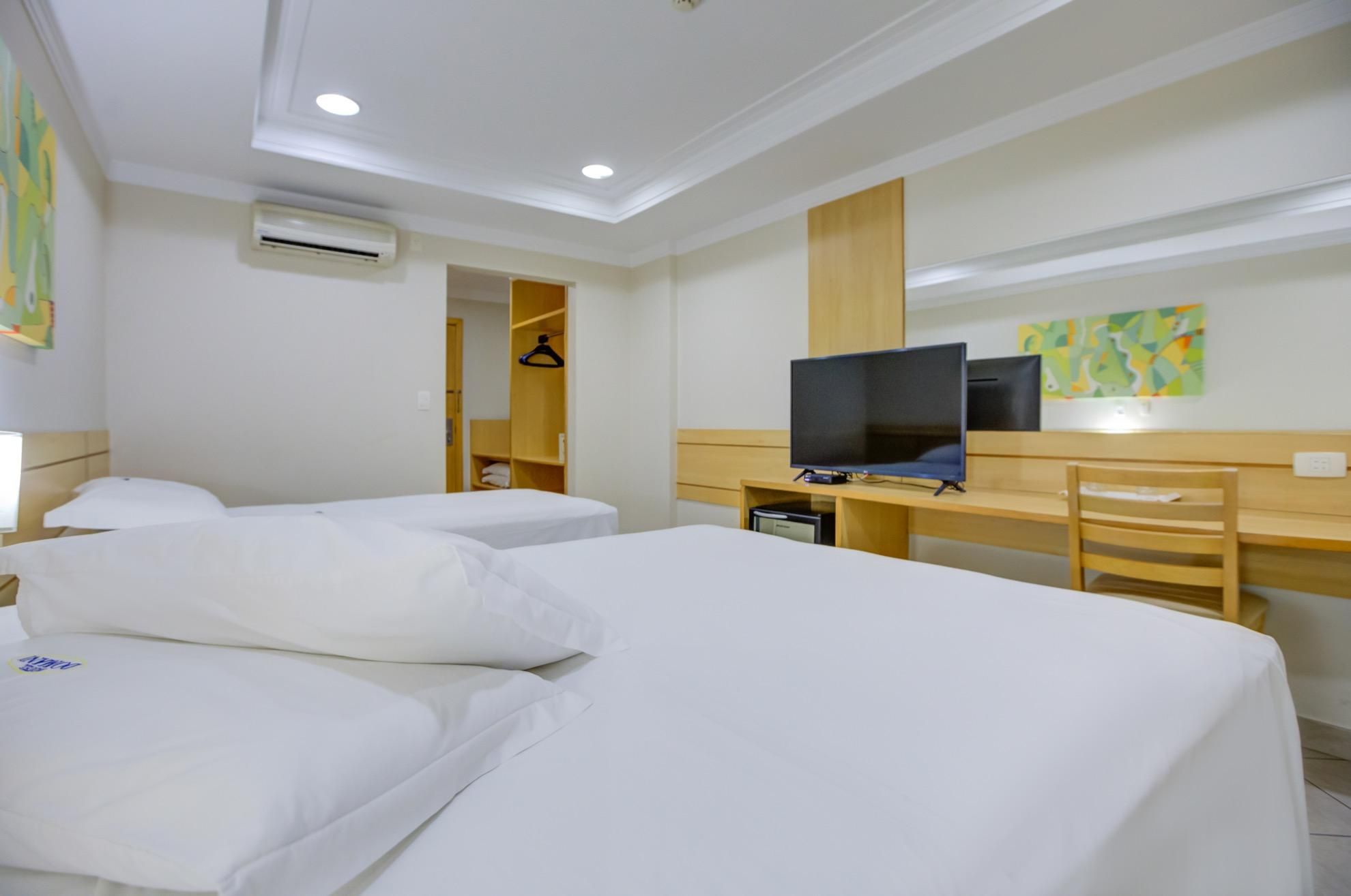 Habitación de hotel con dos camas, un escritorio, un televisor y una silla.
