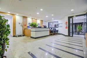 A reception area with a counter, seating, and a plant. - Hotel Domani (Guarulhos)
