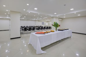 Un salón de conferencias con una larga mesa dispuesta para un bufé, sillas dispuestas en filas y una pizarra en el fondo.