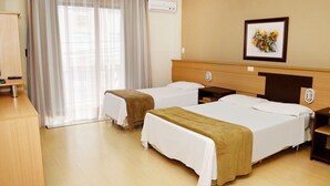 Une chambre d’hôtel avec deux lits, un bureau et une grande fenêtre avec des rideaux légers.