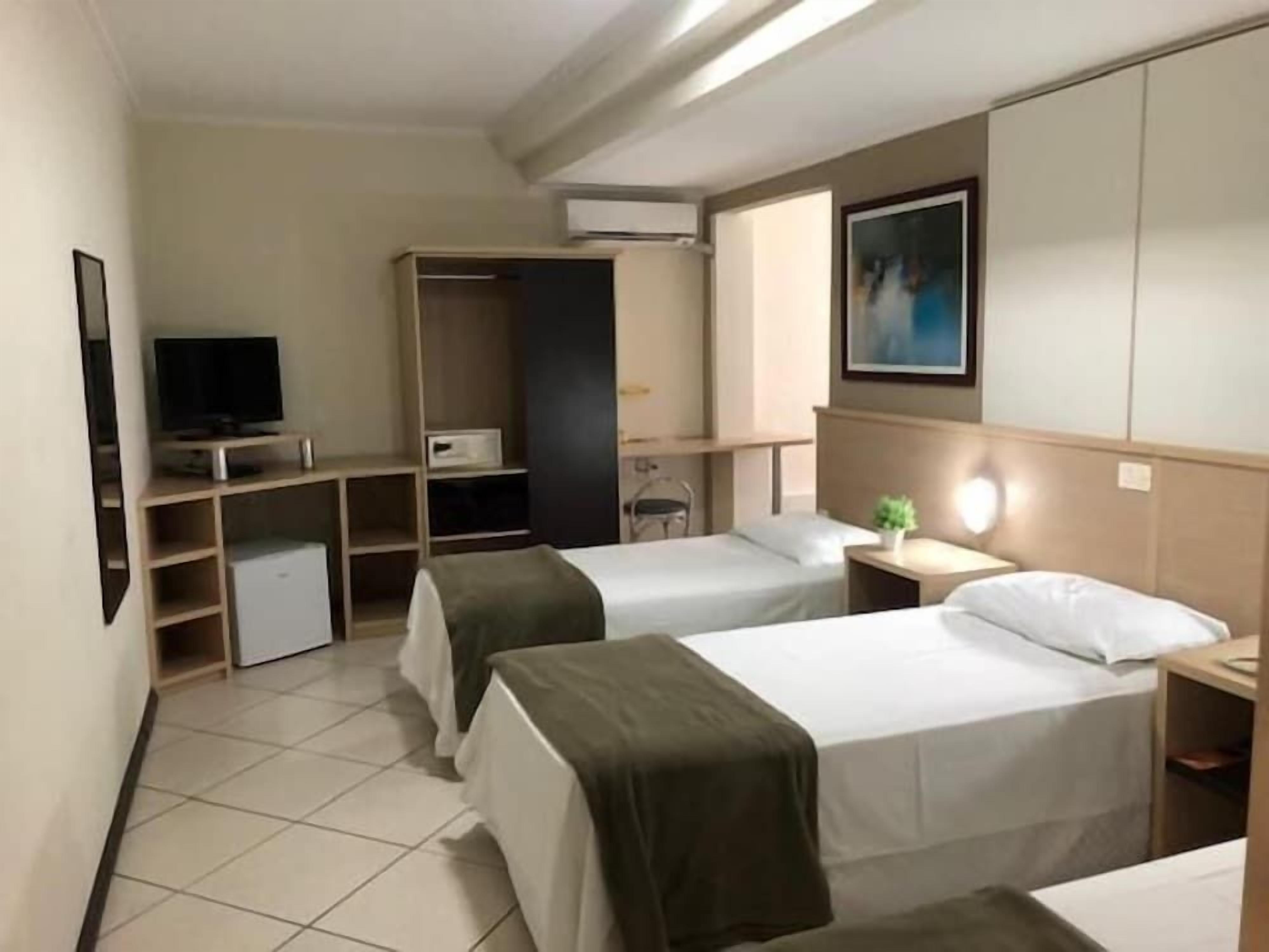 Habitación de hotel con dos camas, televisión, armario y escritorio con lámpara.