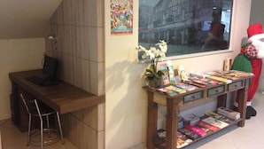 Un espace d’accueil comprenant un bureau en bois, une chaise, un vase avec des fleurs et une table d’exposition où sont présentés des livres et des magazines.