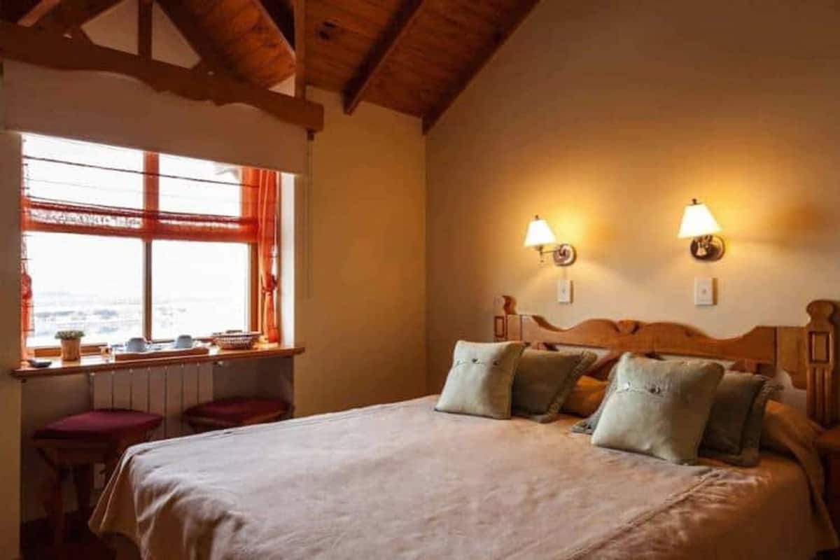 Ein Schlafzimmer mit einem großen Bett, zwei Wandlampen, einem Fenster mit Vorhängen und einer Heizung.