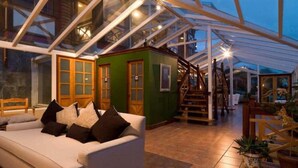 Een orangerie met glazen dak, een groene ruimte, een trap en een witte bank met kussens.