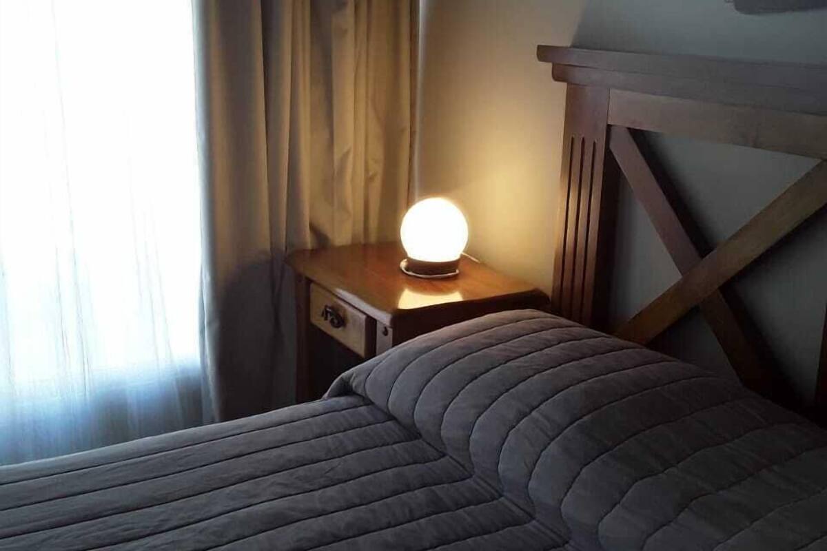 Ein Bett mit einer gestreiften Decke, ein Nachttisch mit Lampe und ein Fenster mit Vorhängen.