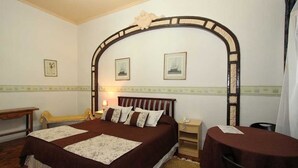 A bedroom with a large bed, a wooden headboard, a bedside table, a nightstand, and a small table with a chair. - Londres 35 Hotel (Santiago)