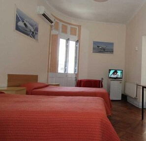 Quarto de hotel com duas camas, televisão e janela com cortinas.