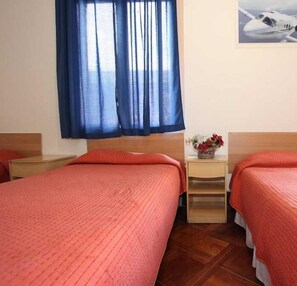 Quarto de hotel com duas camas, uma cabeceira de madeira, uma mesinha de cabeceira com um vaso de flores e um quadro de um avião na parede.