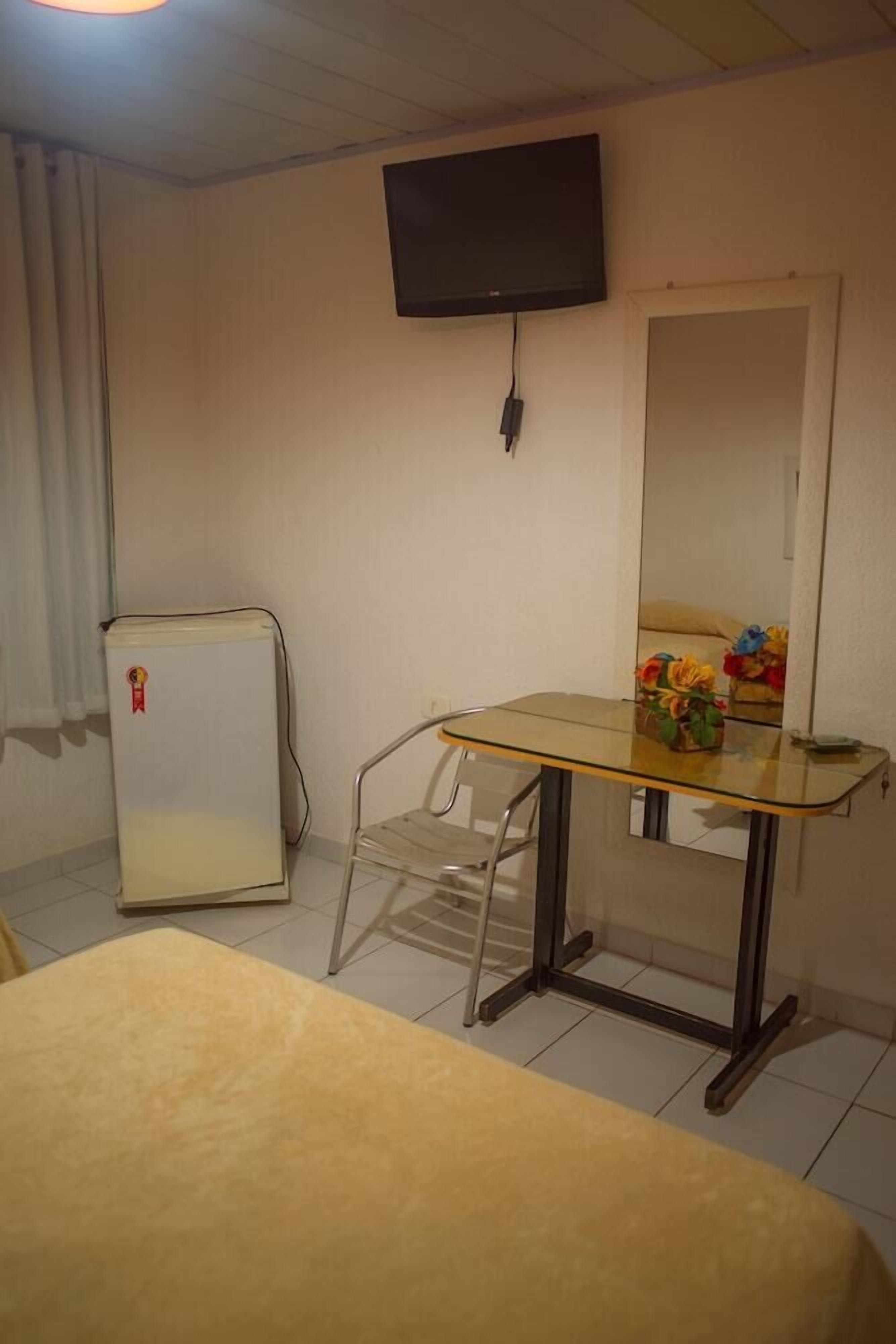 Ein Zimmer mit einem Bett, einem kleinen Tisch, einem Sessel, einem an der Wand befestigten Fernseher und einem Spiegel.
