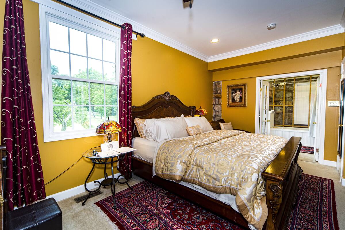 Une chambre à coucher avec un grand lit, une table de chevet, une lampe et une fenêtre avec des rideaux.