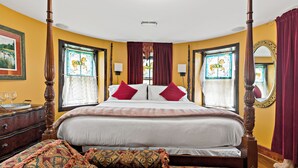 Ein Bett mit Baldachin, ein hölzernes Kopfende, ein großer Spiegel und ein Fenster mit farbigen Glasfenstern.