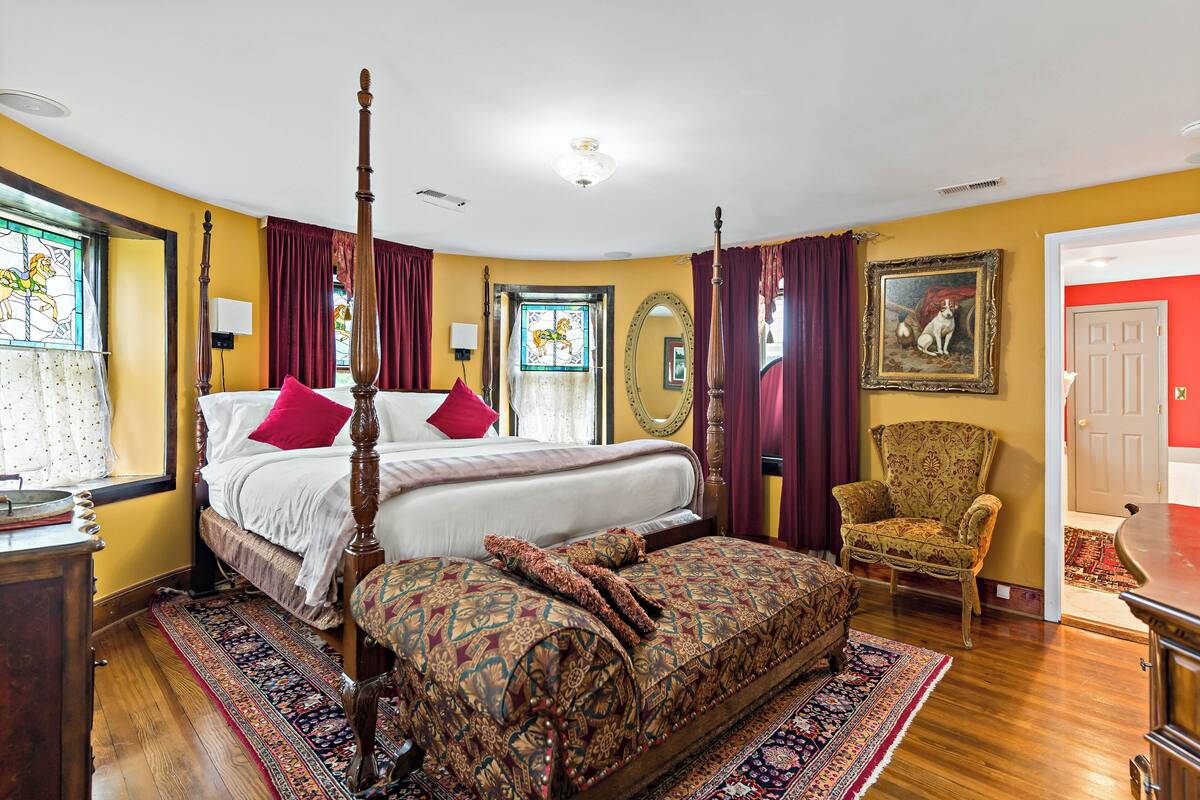 Un lit à baldaquin, un grand miroir, un fauteuil à motifs et une porte rouge.