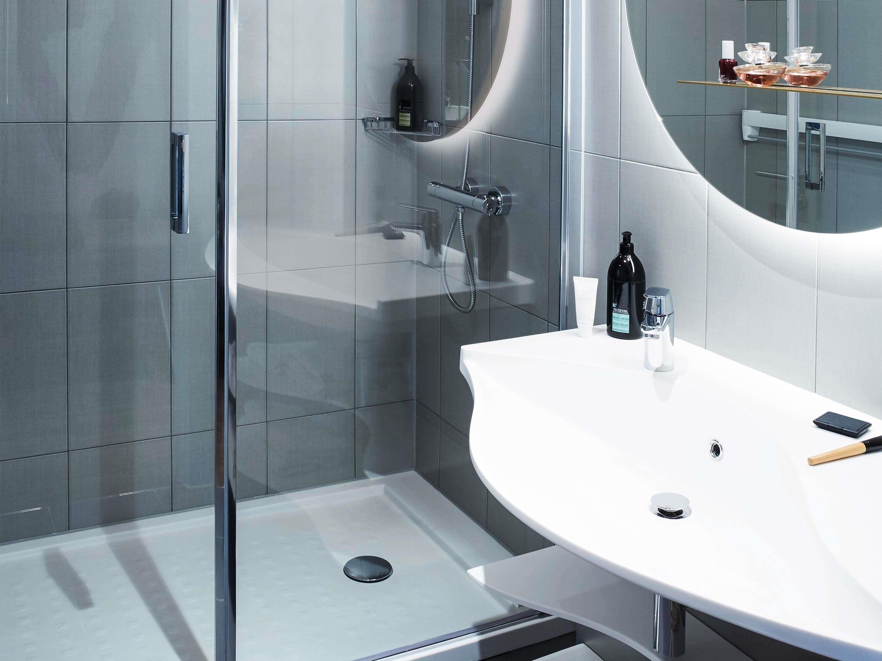 A modern bathroom with a glass shower enclosure, a white sink, and a large mirror.