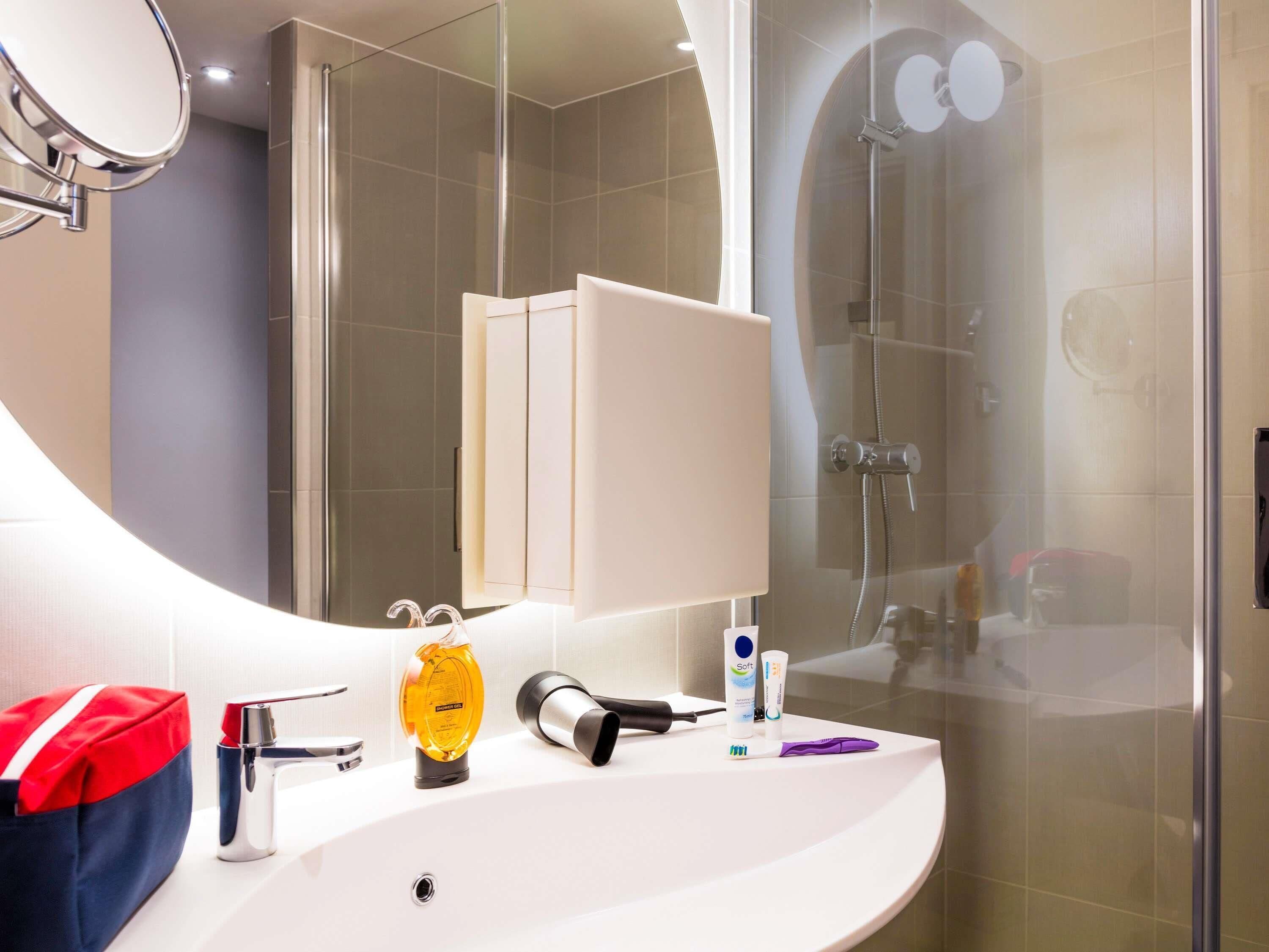 A modern bathroom with a curved sink, a handheld showerhead, a mirror, and a glass shower enclosure.