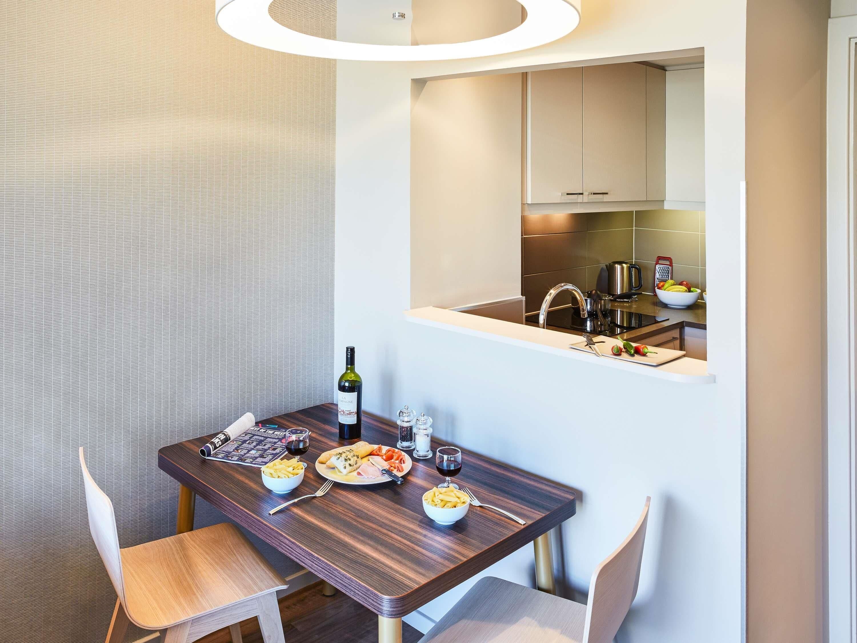 A modern dining area with a wooden table, chairs, and a view of the kitchen through a mirror.