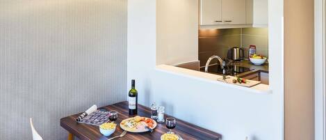 A modern dining area with a wooden table, chairs, and a view of the kitchen through a mirror.