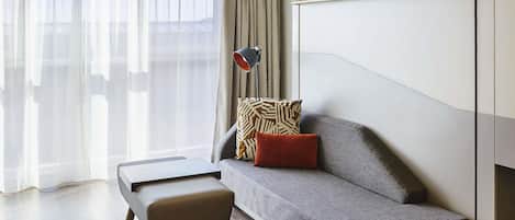 A modern living room with a grey sofa, a small wooden bench, a patterned throw pillow, and a floor lamp.