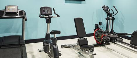 A gym with various exercise equipment including a treadmill, stationary bike, elliptical, and dumbbells.