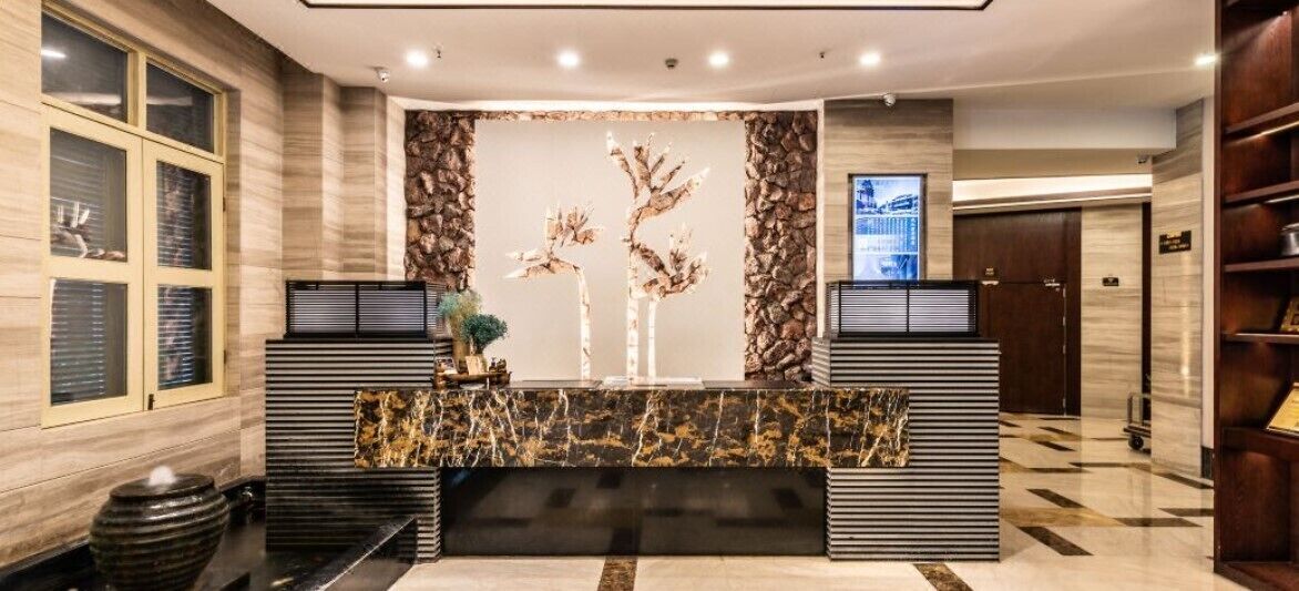 A reception area with a marble counter, a stone wall with a tree sculpture, and a television screen.