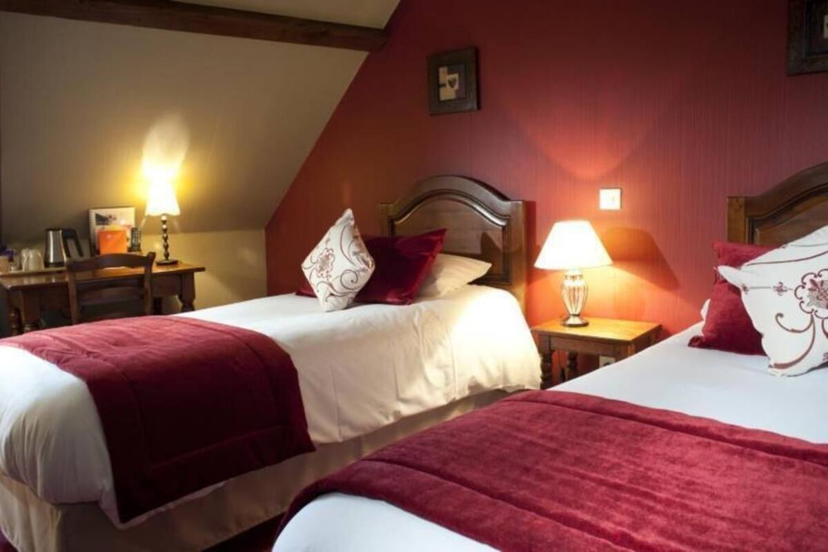 A hotel room with two beds, each with a red blanket, a wooden headboard, and bedside lamps.