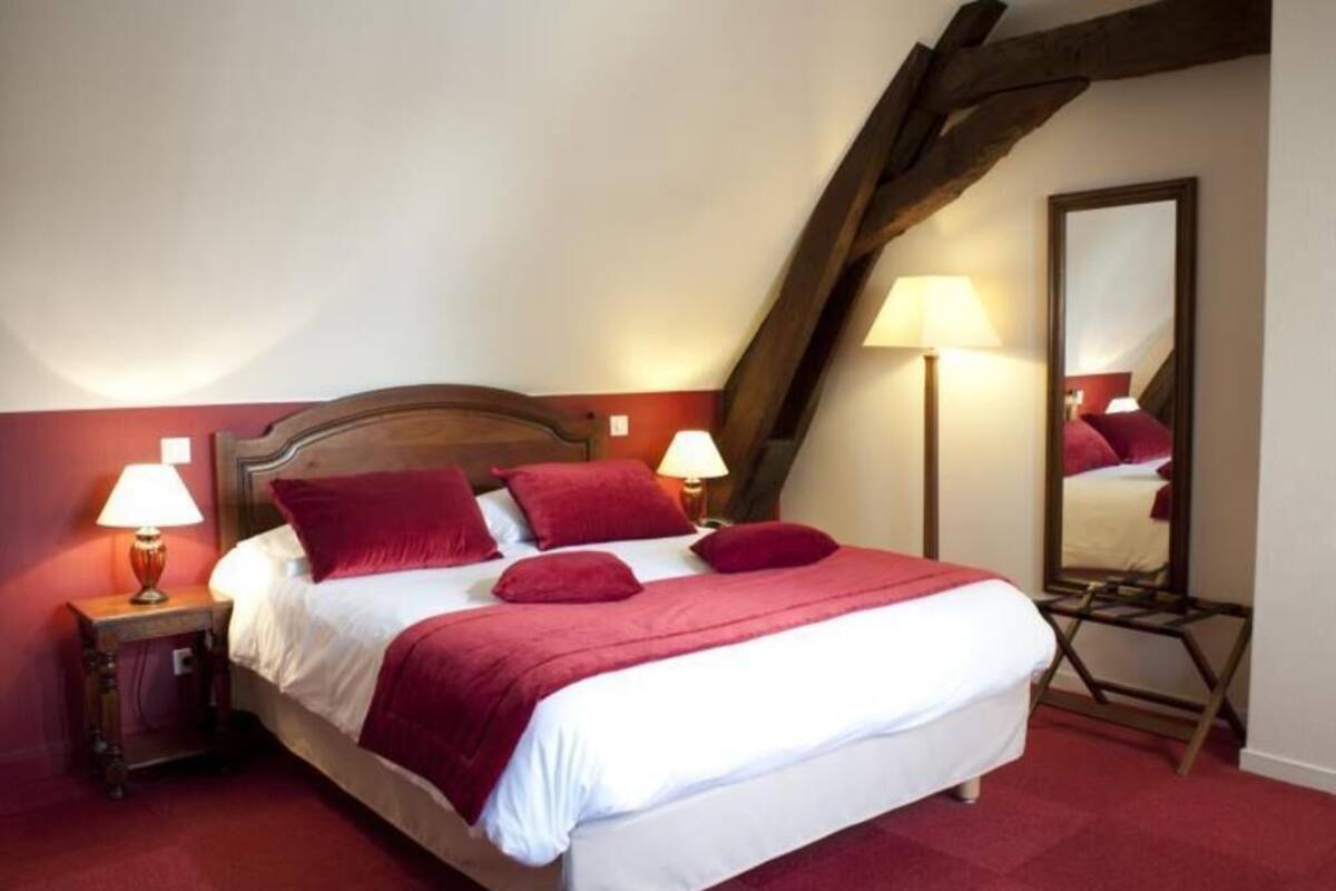 A bedroom with a wooden headboard, a bed with red bedding, two bedside lamps, a mirror, and a red carpet.