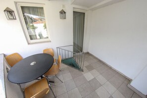 A balcony with a table and chairs, a window with curtains, and a door with a view of a building. - Hotel Hayat (Sarajevo)