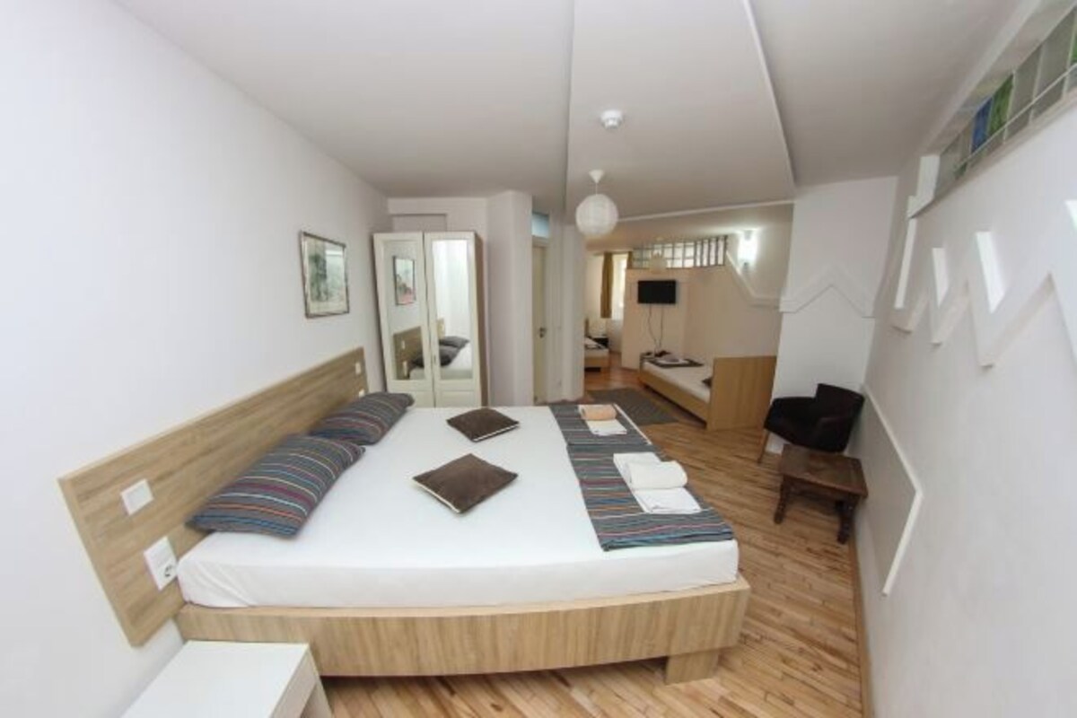 A modern bedroom with a wooden bed, a bedside table, a chair, and a TV in the background.
