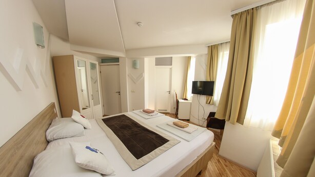 A hotel room with a large bed, a flat-screen TV, a desk with a chair, and a window with curtains.