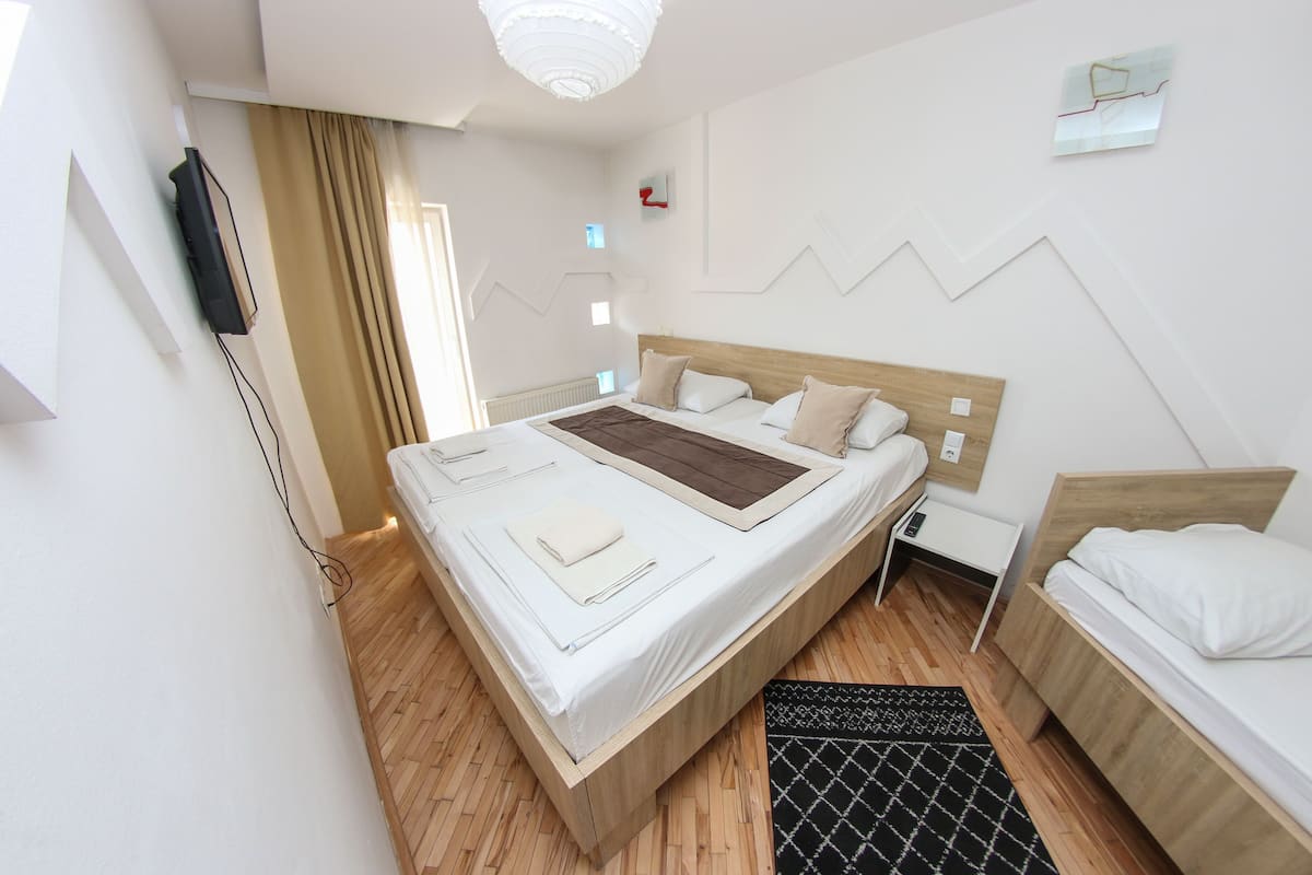 A modern hotel room with a large bed, a smaller bed, a desk, and a TV mounted on the wall.