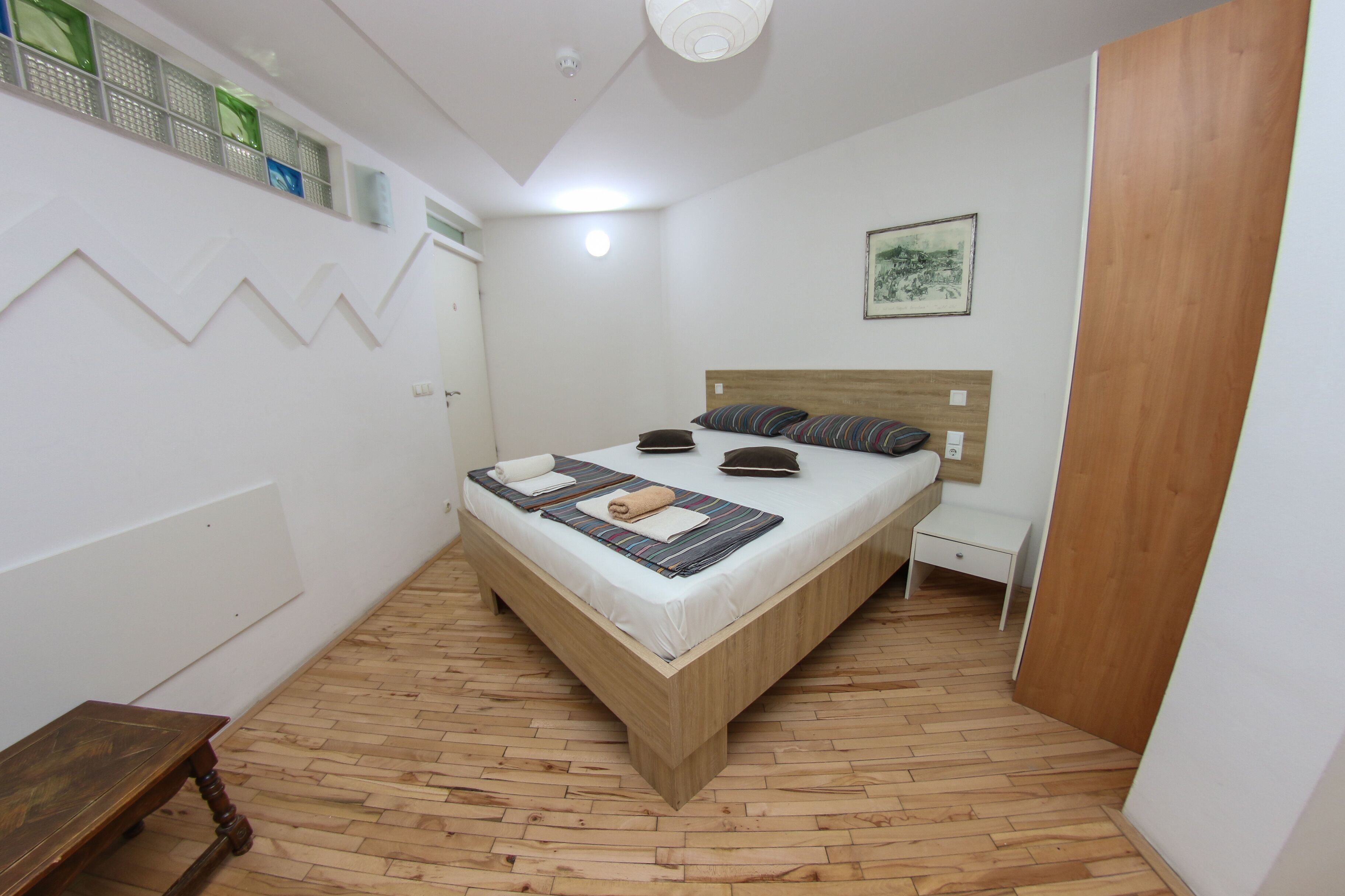 Ein kleines, ordentlich eingerichtetes Schlafzimmer mit einem Holzbett, einem Nachttisch und einer kleinen Bank.