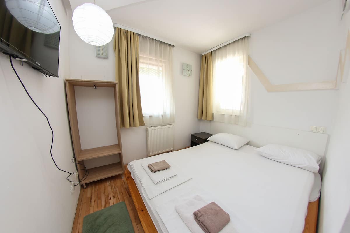 A bedroom with a bed, a wardrobe, a nightstand, a TV, and a window with curtains.