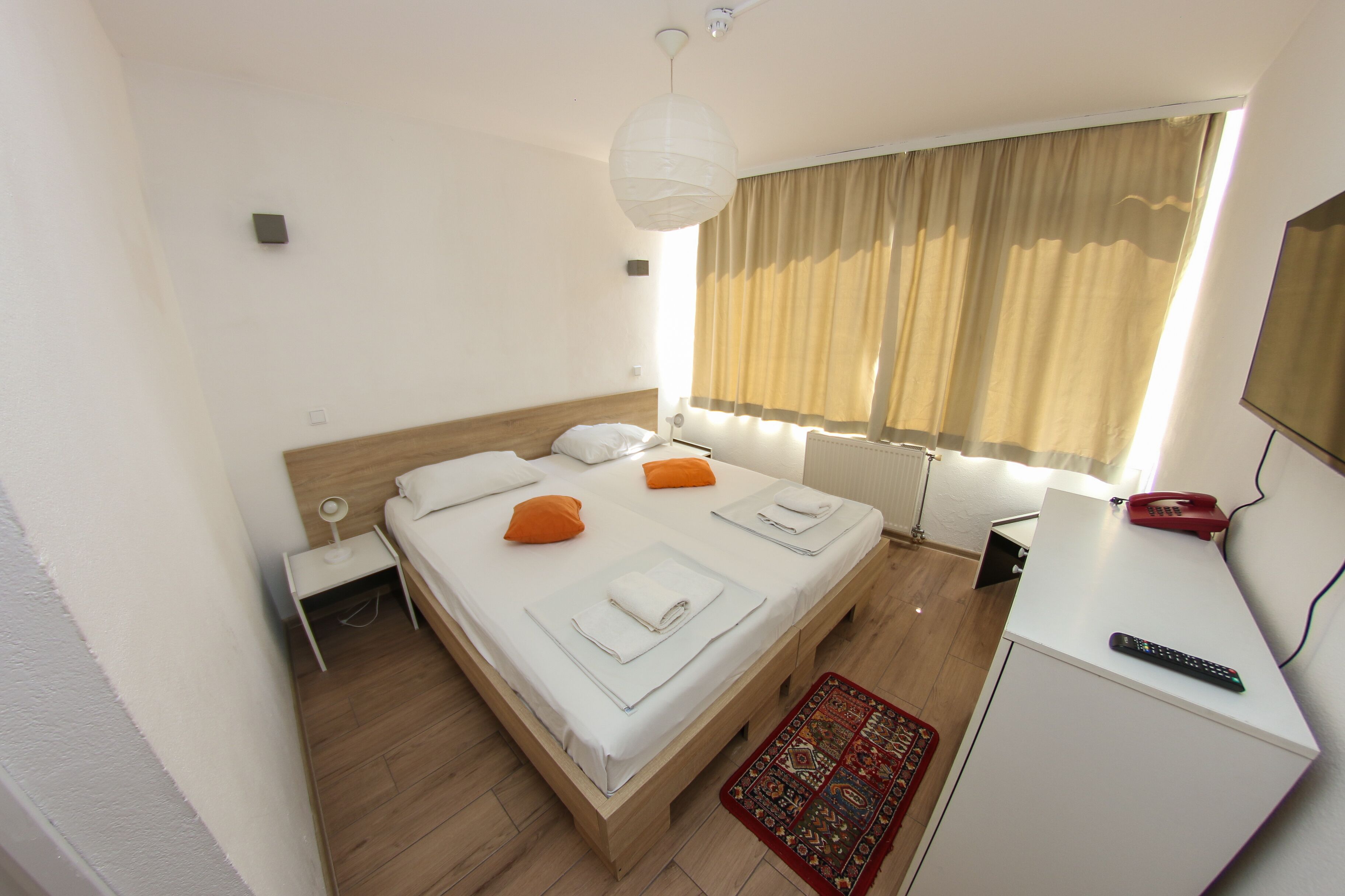 Ein Hotelzimmer mit Bett, Nachttisch, Lampe und Schreibtisch mit Telefon und Fernbedienung.