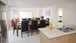 A modern kitchen with a dining area, featuring a large table, chairs, and a kitchen island with a sink. - Stoneyfell (POINT COOK)