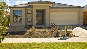 A modern single-story house with a garage, a front door, and a small garden area with plants and a bench. - Stoneyfell (POINT COOK)