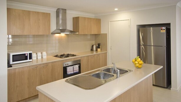 A modern kitchen with wooden cabinets, a stainless steel refrigerator, a microwave, and a sink with a built-in grill. - Stoneyfell (POINT COOK)