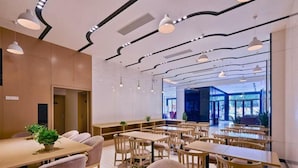Un comedor moderno con mesas y sillas de madera, iluminación colgante y vistas al exterior.