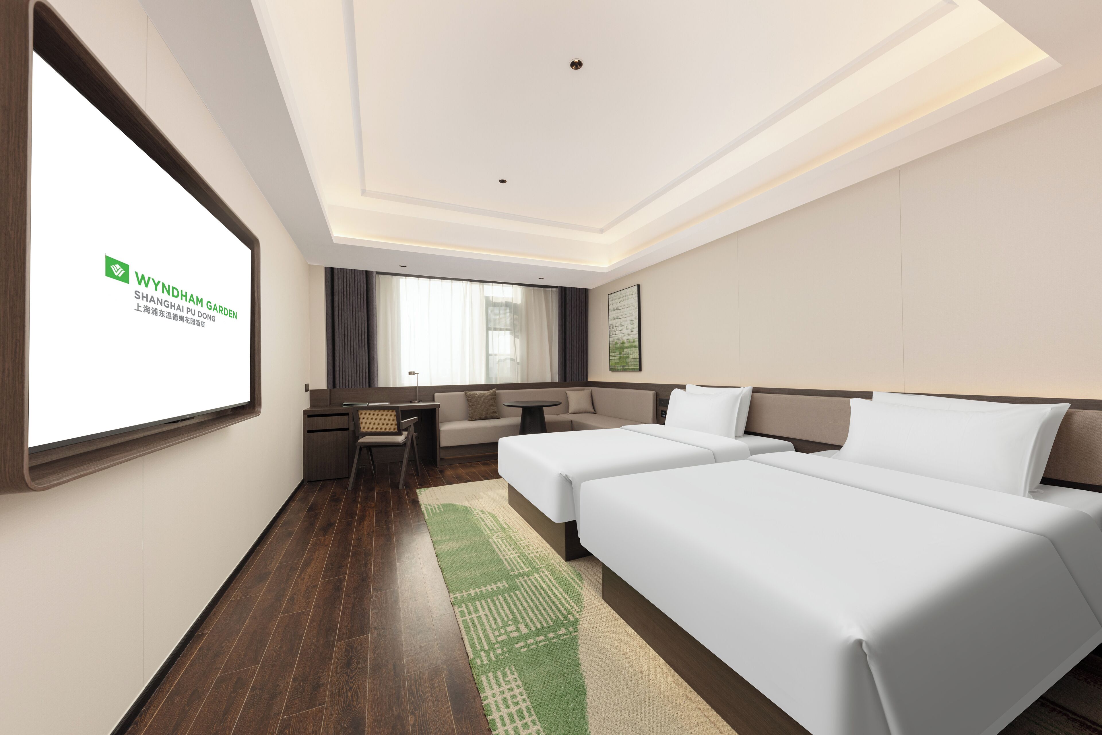 A hotel room with two beds, a sofa, a small table, and a TV screen displaying the hotel's name.