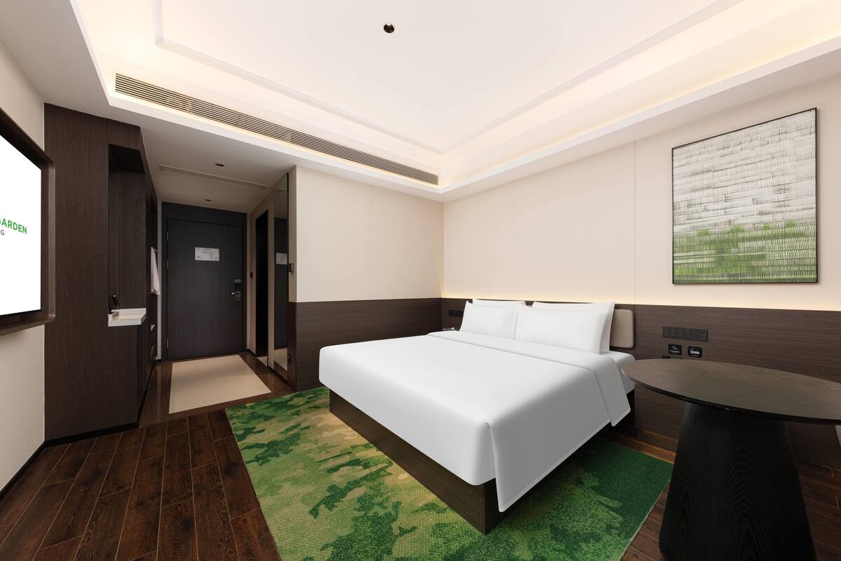 Une chambre d’hôtel avec un lit, un bureau, un tapis vert et un tableau au mur.