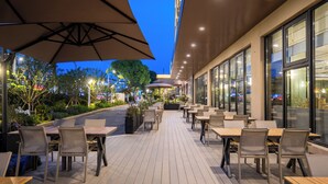 An outdoor patio with tables and chairs, surrounded by plants and trees, under large umbrellas. - Wyndham Garden Shanghai Pudong (Shanghai)