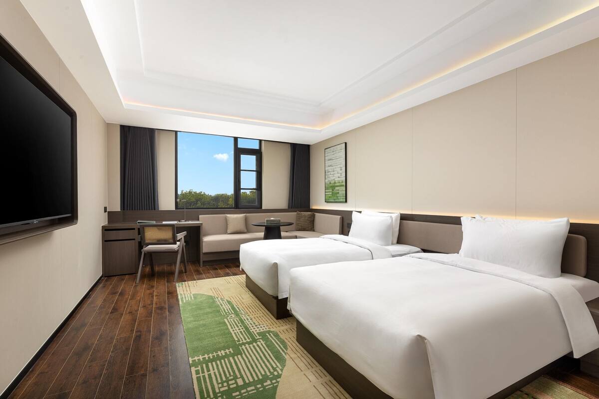 Une chambre d’hôtel avec deux lits, un bureau, une chaise, une télévision et une grande fenêtre.