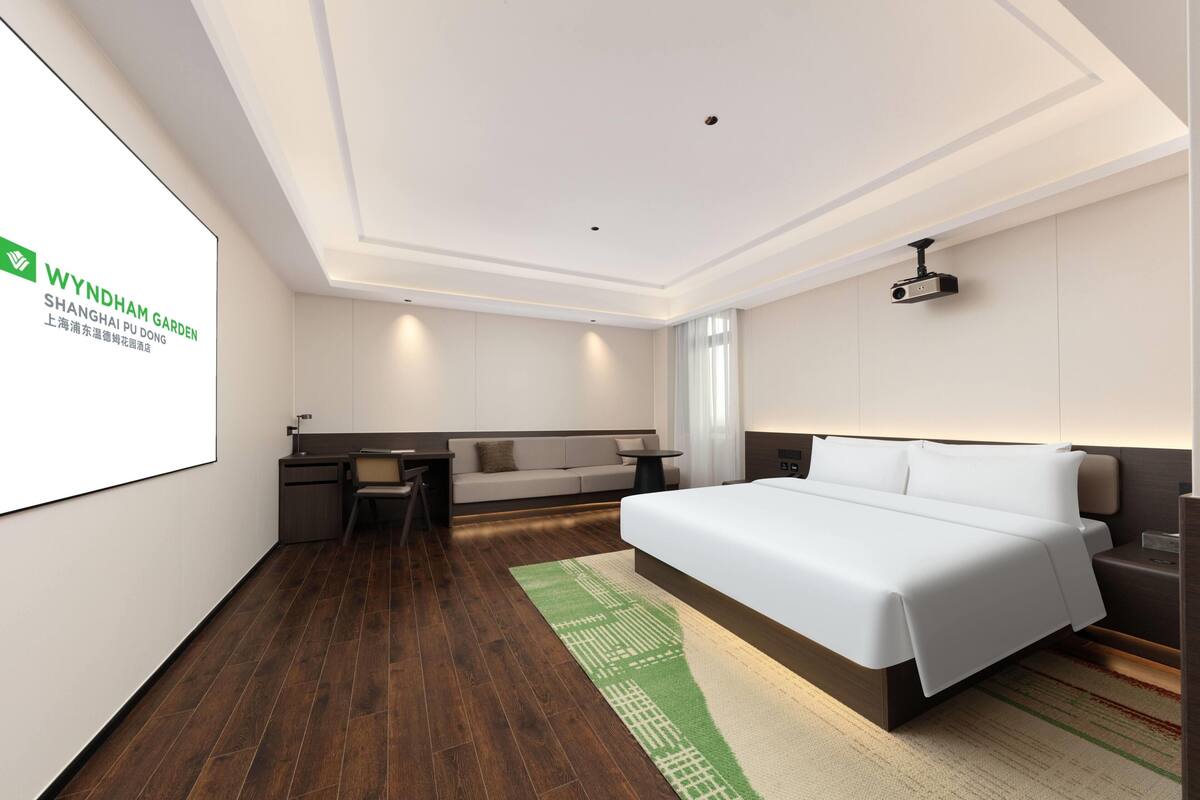 Une chambre d’hôtel équipée d’un lit, d’un bureau, d’un canapé et d’un écran de projection.
