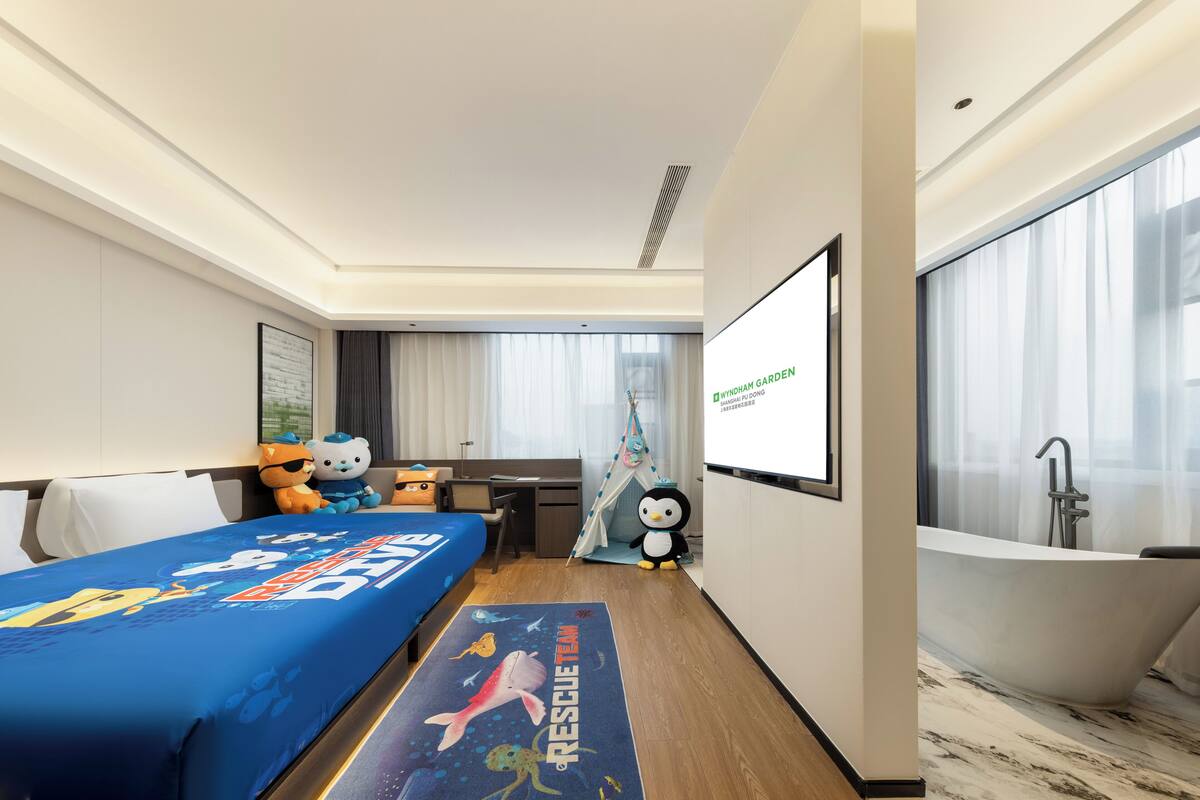 Une chambre d’hôtel équipée d’un lit, d’un bureau, d’une grande fenêtre, d’une baignoire et d’un écran affichant le nom « Wyndham Garden ».