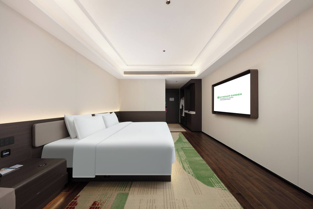 Une chambre d’hôtel moderne dotée d’un grand lit, d’un téléviseur à écran plat fixé au mur et d’un plancher en bois.