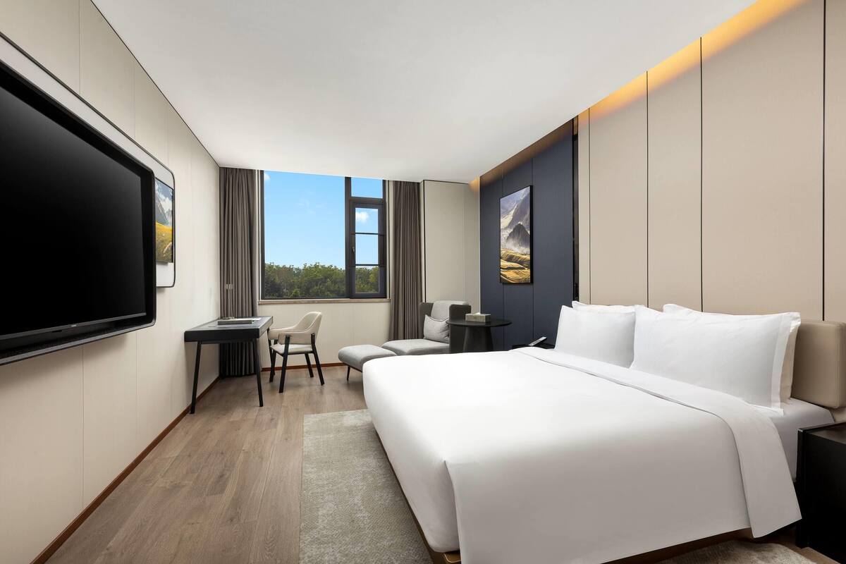 Une chambre d’hôtel avec un grand lit, un bureau, une chaise, une télévision et une fenêtre donnant sur un beau paysage.
