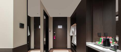 A hotel corridor with a wooden floor, a white wall, a door with a pink lock, and a counter with a coffee maker and a water dispenser.