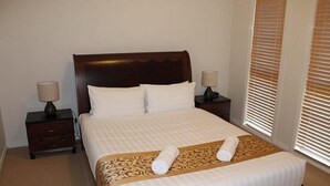 A neatly made bed with a patterned bedspread, two pillows, and two bedside lamps. - City Cottage (GOWANBRAE)