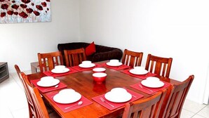 A dining table set with white plates and red placemats, surrounded by wooden chairs. - City Cottage (GOWANBRAE)