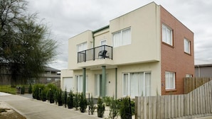 A modern two-story apartment building with a balcony, a concrete driveway, and a wooden fence. - City Condo (GOWANBRAE)